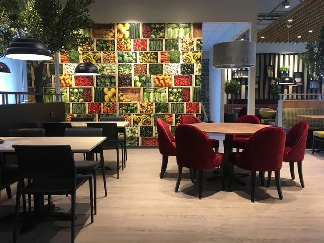 Coop Cafe Rudshøgda: åpen spisesal med røde stoler, runde bord og et veggmotiv av frukt og grønnsaker