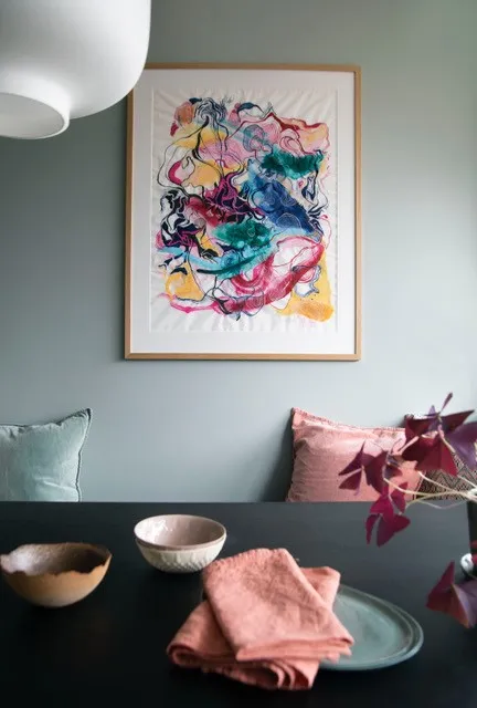 Sofa med puter under et fargerikt kunstverk mot en blågrå vegg