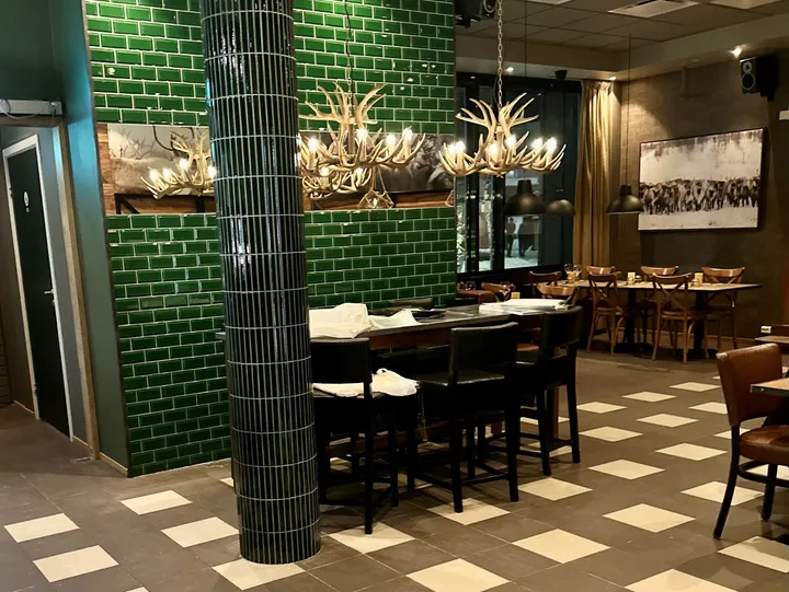 Crosta Restaurant Alta: spisesal med grønn flislagt søyle og vegg, takkroner av gevir og sjakkmønstret gulv